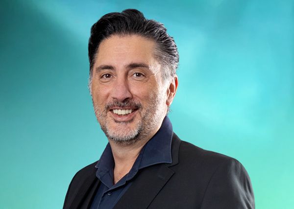 Geschäftsführer Dabiel Raseghi in dunklem Anzug vor blau-grünem Hintergrund