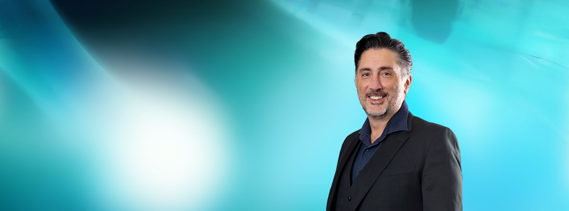 Geschäftsführer Dabiel Raseghi in dunklem Anzug vor blau-grünem Hintergrund