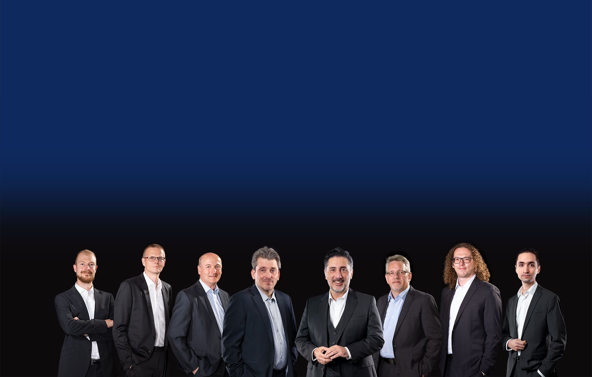Gruppe von acht Männern in Anzügen vor schwarzem Hintergrund, in der Mitte E+H CEO Daniel Raseghi