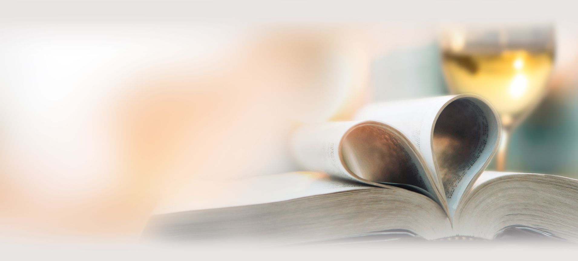 Aufgeschlagenes Buch mit zwei zu einem Herz geformten Seiten und einem Glas Weißwein im Hintergrund - DART