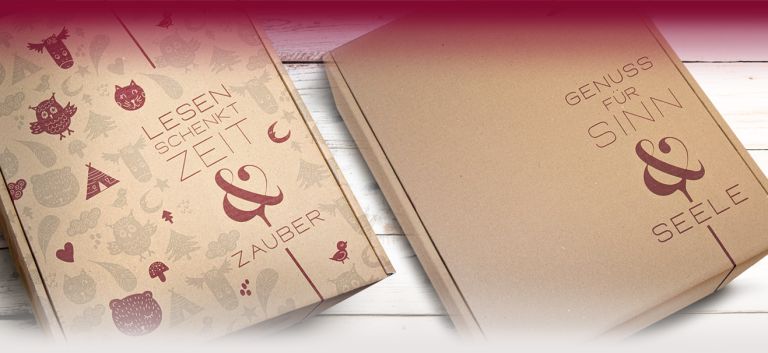 Zwei Pappverpackungen mit Schriftzügen 'LESEN SCHENKT ZEIT & ZAUBER' und 'GENUSS FÜR SINN & SEELE' auf hellem Holzhintergrund - DART